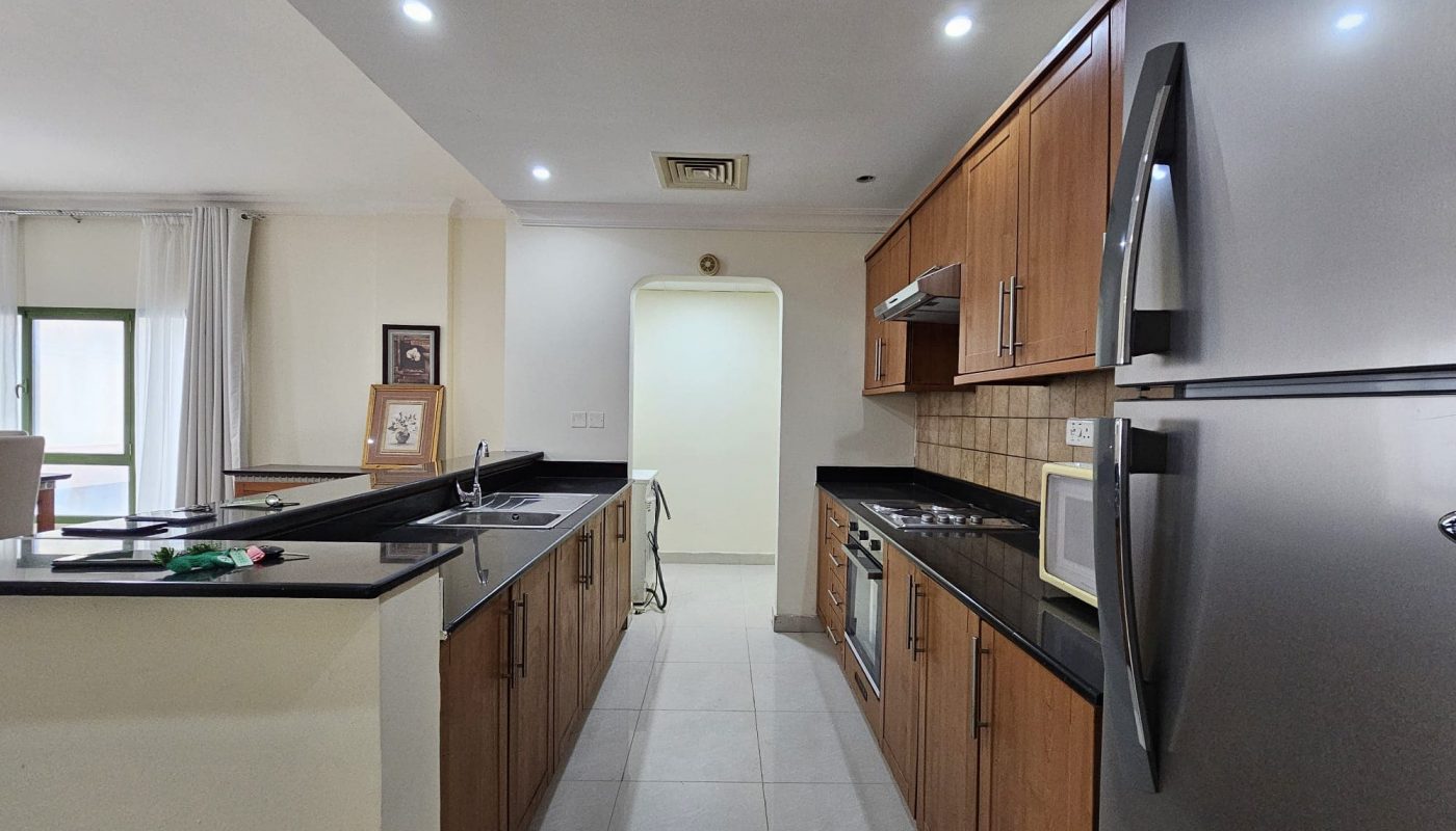 A well-lit, modern kitchen with wooden cabinets, stainless steel appliances, and a central island graces this 2BR Apartment for rent in Juffair.