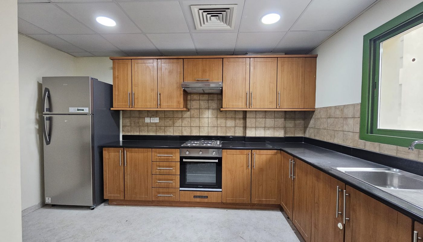 A modern 3 BR apartment for rent in Juffair with a kitchen interior featuring wooden cabinets, stainless steel appliances, and tiled countertops.