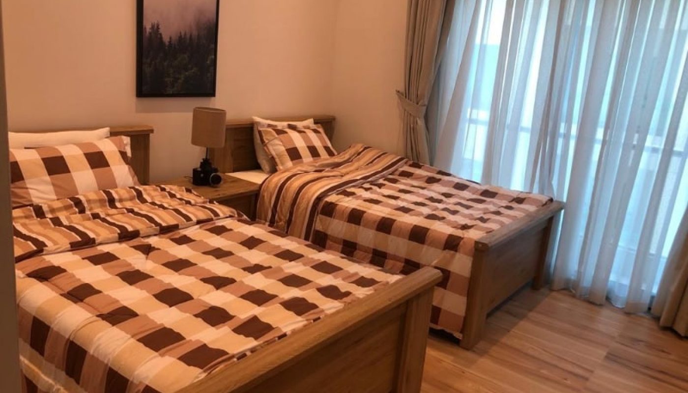 A tidy bedroom with two single beds covered in checkered bedding, wooden floors, and sheer curtains. Auto Draft