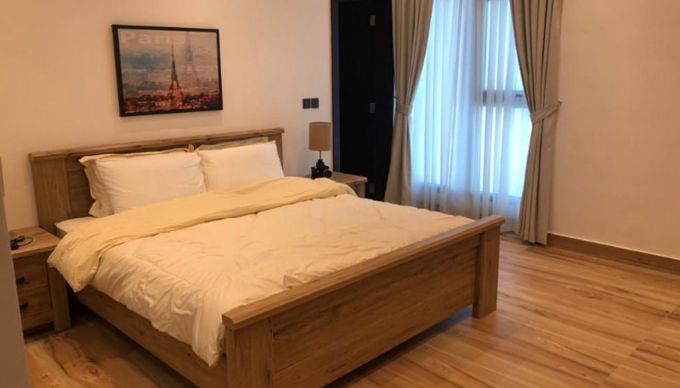 A neatly made bed in a tidy bedroom with a Paris-themed auto draft picture on the wall.