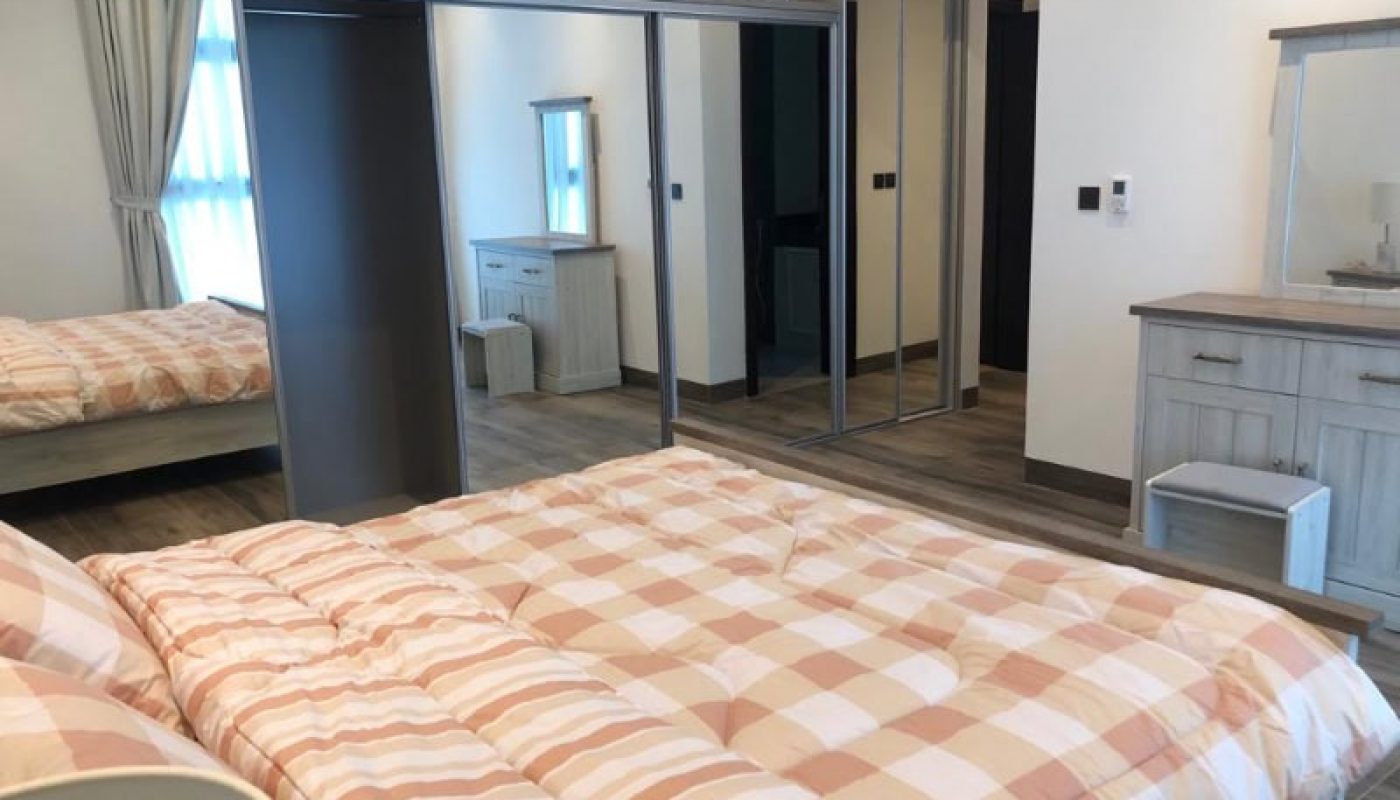 Modern bedroom with a large bed, mirrored wardrobe, and an en-suite bathroom visible in the background.