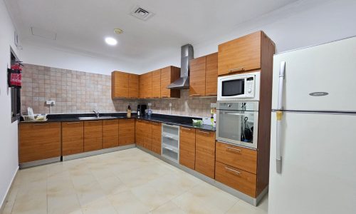 Modern kitchen interior with wooden cabinets, stainless steel appliances, and tiled floor in a fully-furnished, TWO BEDROOM apartment in Juffair.