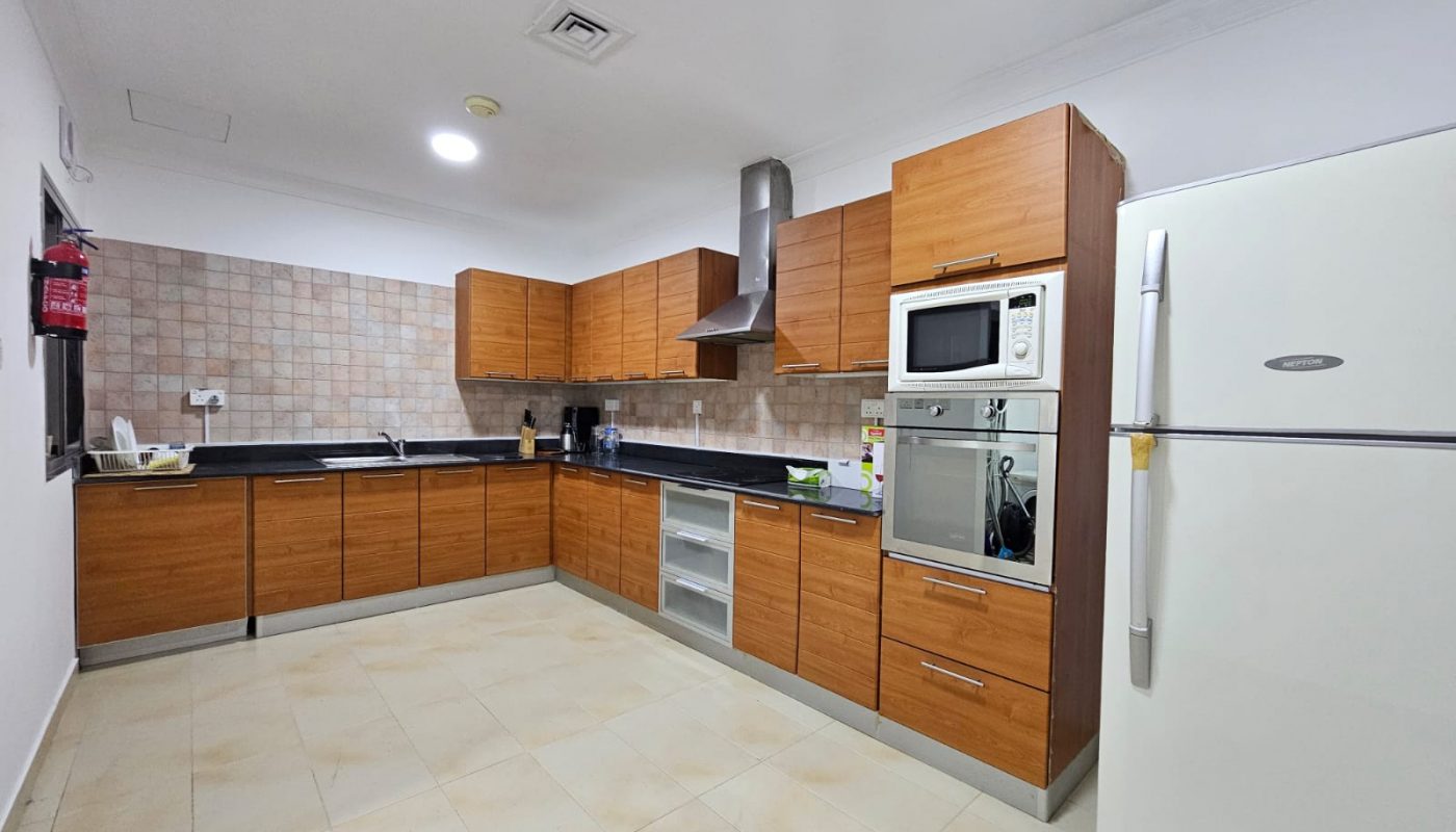 Modern kitchen interior with wooden cabinets, stainless steel appliances, and tiled floor in a fully-furnished, TWO BEDROOM apartment in Juffair.