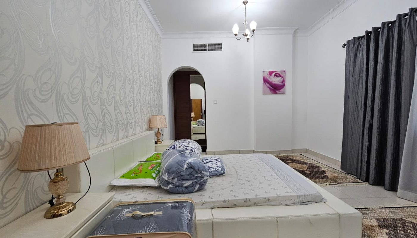 A neatly arranged two-bedroom apartment in Juffair with a fully-furnished bedroom, patterned wallpaper, and a small play mat for children.
