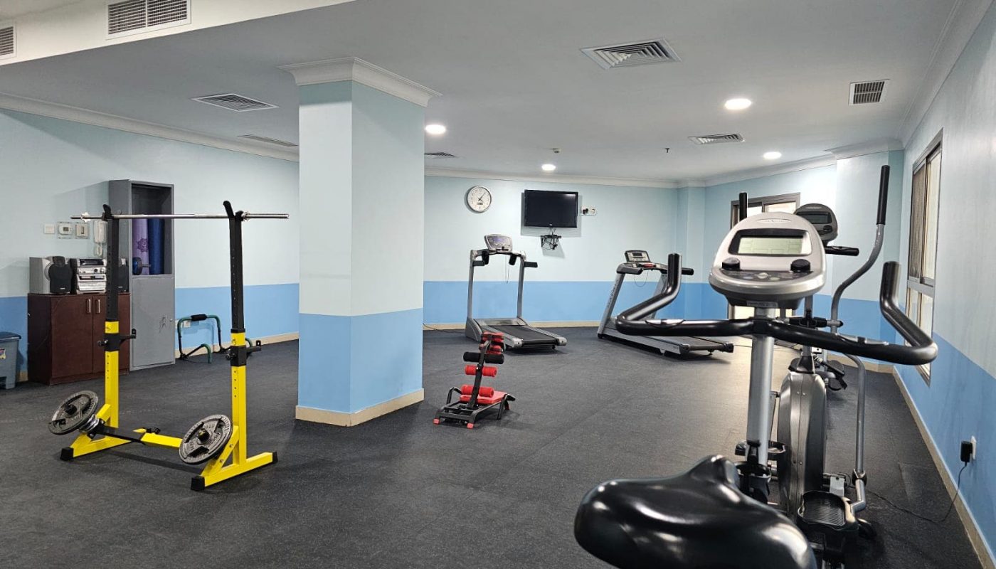 Interior of a modern gym in a fully-furnished two-bedroom apartment in Juffair with various exercise equipment.