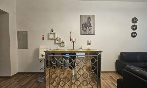 An elegant apartment for rent in Juffair featuring a modern living room with a geometric-patterned gold coffee table, white chairs, decorative artwork, and a dark blue sofa.