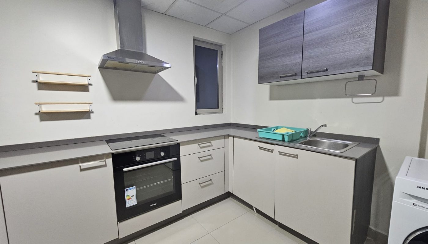 An elegant apartment for rent in the Juffair area, featuring a modern kitchen with stainless steel appliances, white cabinetry, and wooden shelves.