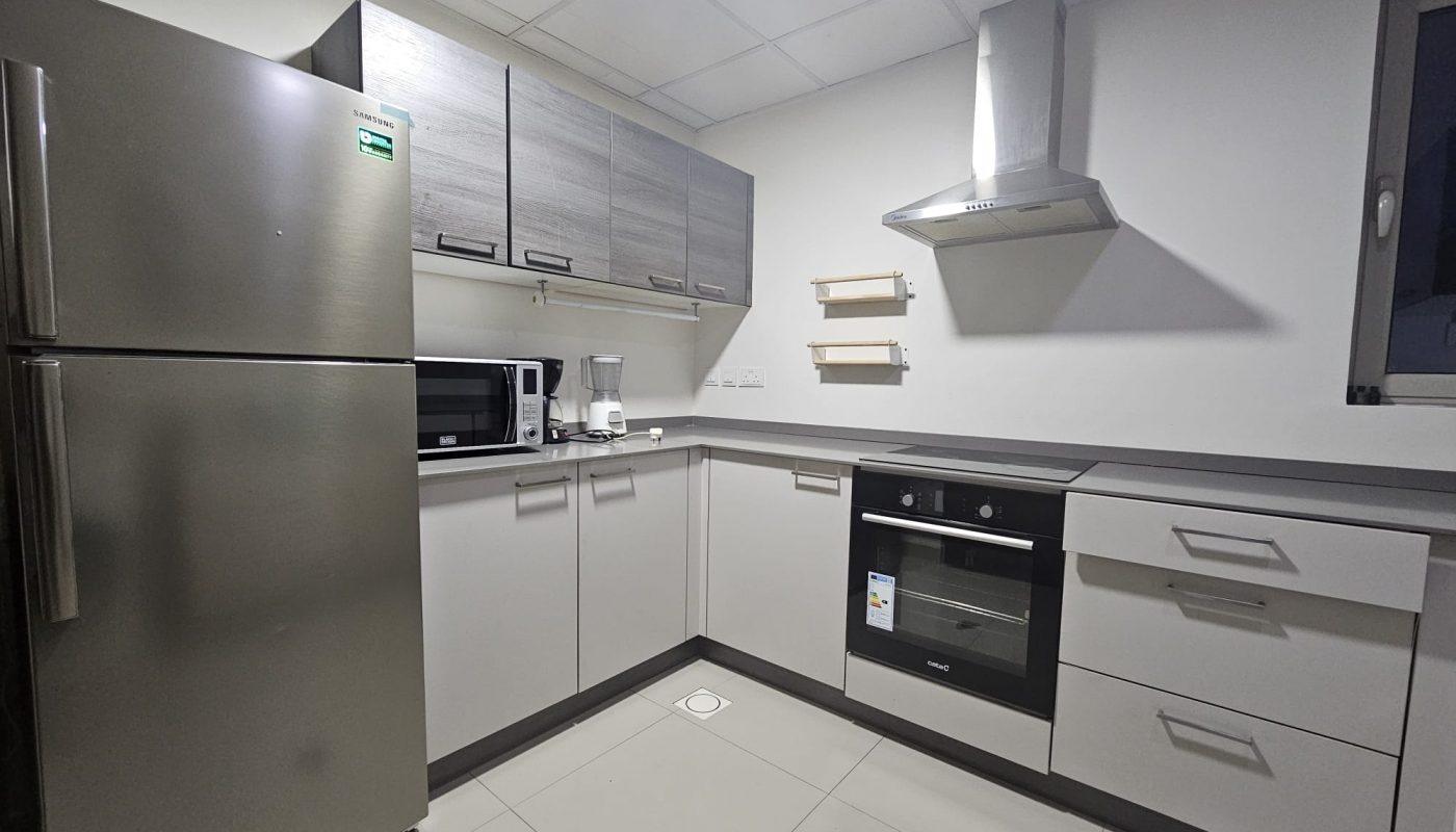 Elegant apartment in the Juffair area with a modern kitchen interior, stainless steel appliances, white cabinetry, and a range hood available for rent.