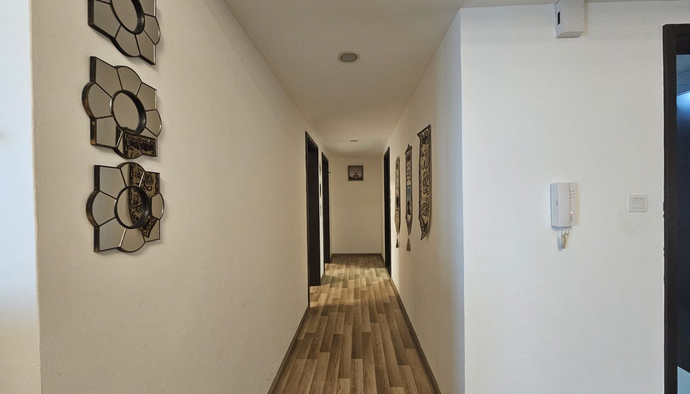 An elegant modern hallway in a residential apartment featuring wooden flooring, white walls with decorative mirrors, and framed artwork.