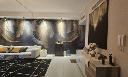 Modern living room interior in a flat for rent featuring a large feather-themed wall mural, contemporary furniture, and decorative accents in Juffair.