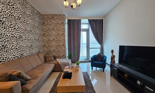 Modern living room in a Juffair apartment with leopard print wallpaper, a beige sectional sofa, black television stand, wooden coffee table, and a blue armchair.