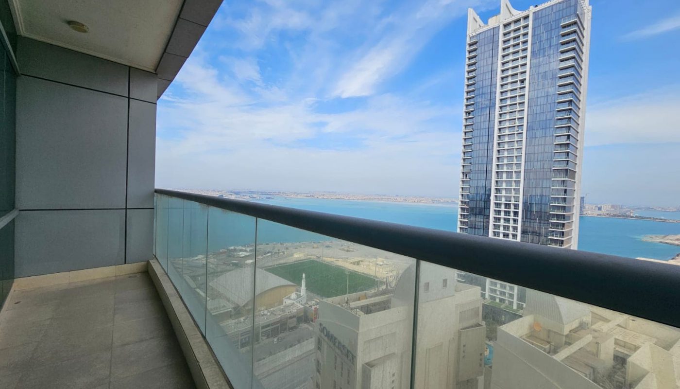 Balcony view of a cityscape with a skyscraper and water body in the distance from a Juffair apartment for rent.