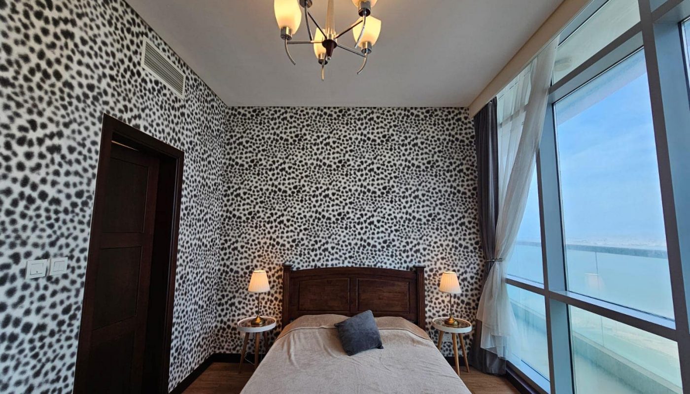 An apartment in Juffair with a bedroom featuring leopard print wallpaper, a large bed, two bedside tables with lamps, and a window offering an ocean view.