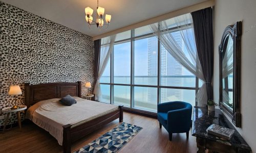 Modern apartment bedroom for rent in Juffair with animal print wallpaper, wooden furniture, and a floor-to-ceiling window offering a city view.