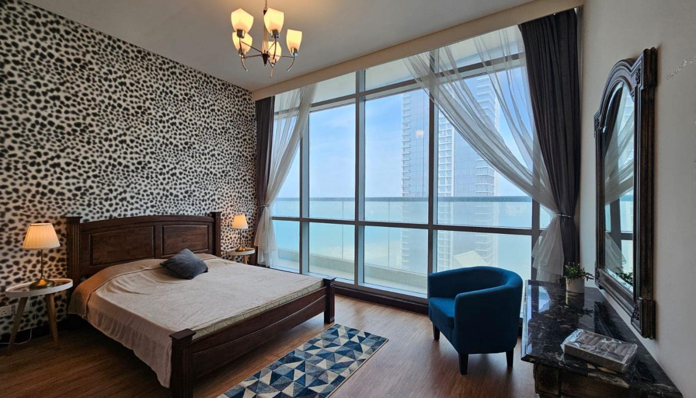 Modern apartment bedroom for rent in Juffair with animal print wallpaper, wooden furniture, and a floor-to-ceiling window offering a city view.