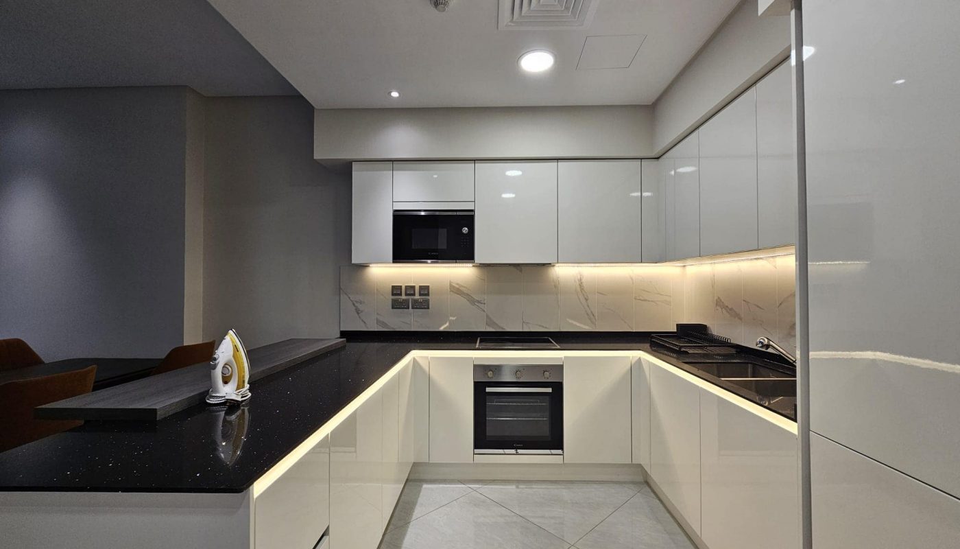 Modern kitchen interior with built-in appliances, black countertops, and led lighting under white cabinets.