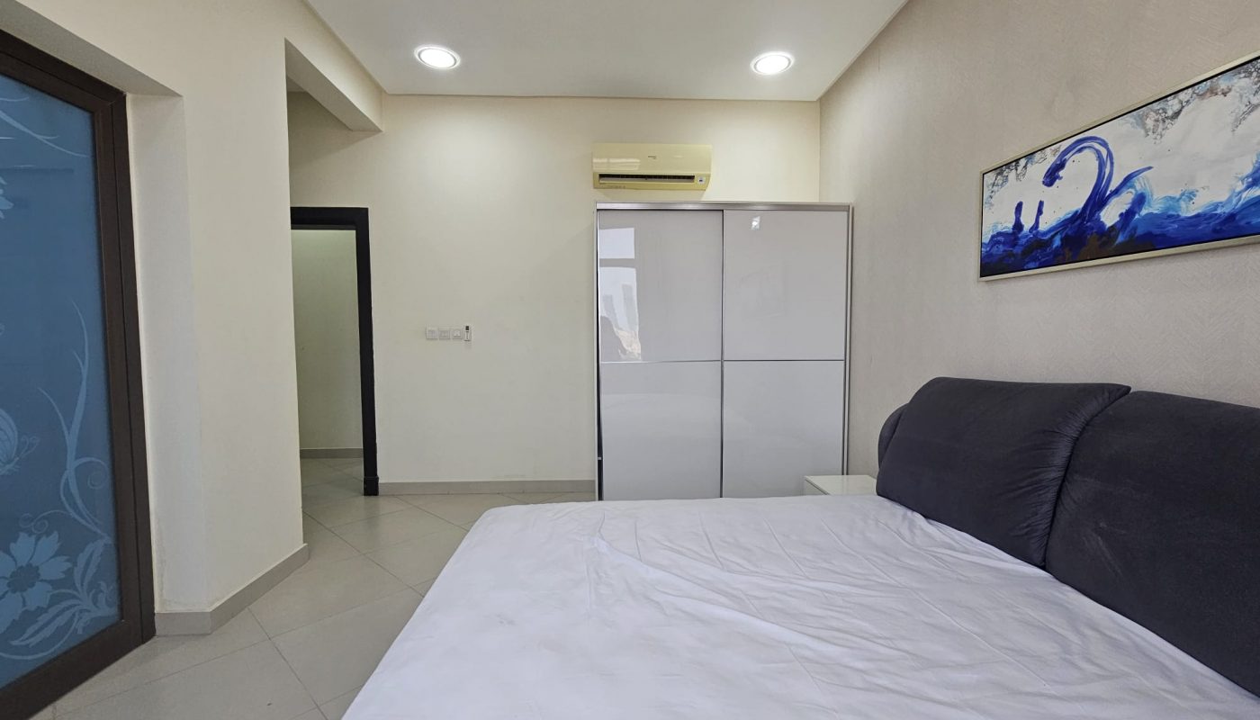 A bright, modern 2BR furnished flat bedroom with a large bed, minimalistic decor, and abstract art on the walls.