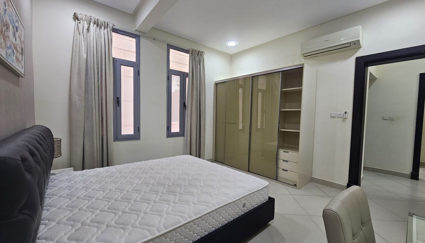 A modern 2BR flat in Adliya, furnished with a large bed, built-in wardrobes, split air conditioning, and neutral color tones. Internet included.