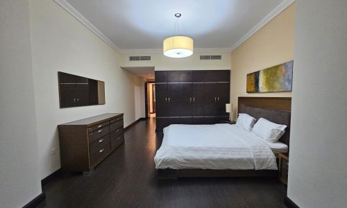 Modern 3BR apartment bedroom with a large bed, wooden furniture, and minimalistic decor.