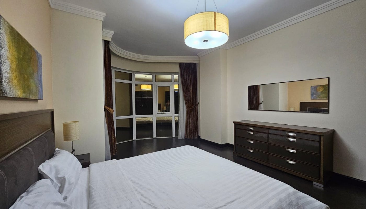 Modern 3BR apartment bedroom with a large bed, contemporary furnishings, and an attached balcony.