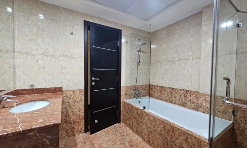 A modern 3BR apartment bathroom interior with marble tiles, featuring a sink, bathtub, and glass shower enclosure.