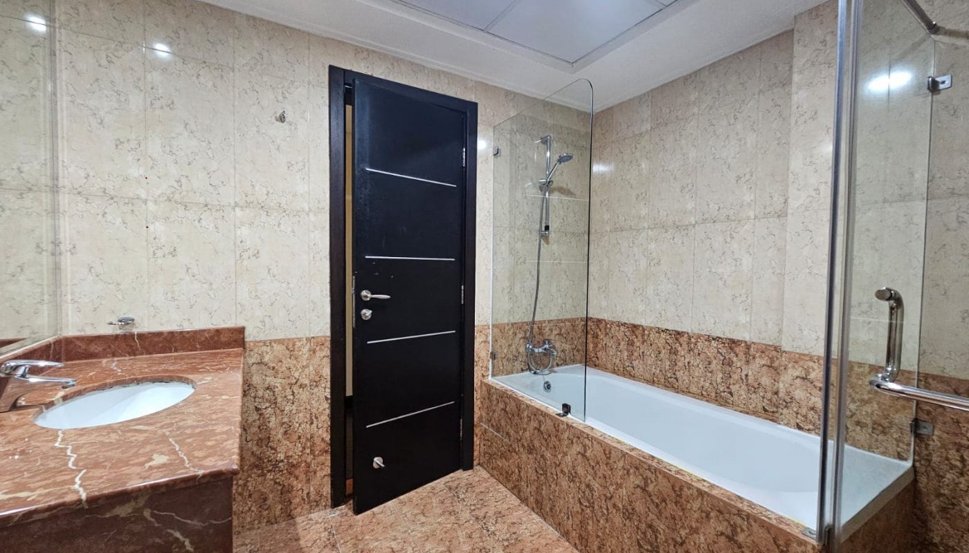A modern 3BR apartment bathroom interior with marble tiles, featuring a sink, bathtub, and glass shower enclosure.
