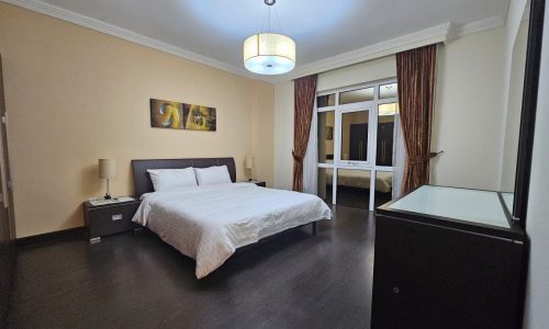 A neatly arranged, modern 3BR apartment bedroom with a large bed, bedside tables, and warm lighting.