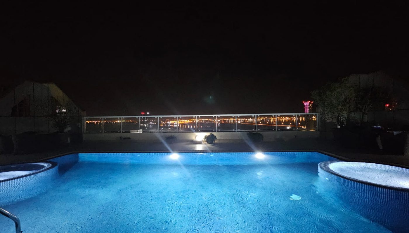 An illuminated swimming pool at night with modern 3BR apartment buildings in the background.
