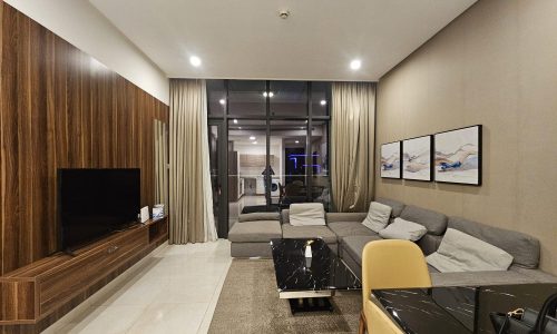 Modern living room with a gray sofa, armchair, black marble coffee table, mounted tv, and wooden panels, leading to a balcony with curtains.