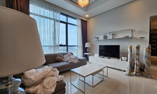 Modern living room with an unmade sofa, glass coffee table, white tv stand, and a large window with ocean view in a fully-furnished 2 bedroom apartment.