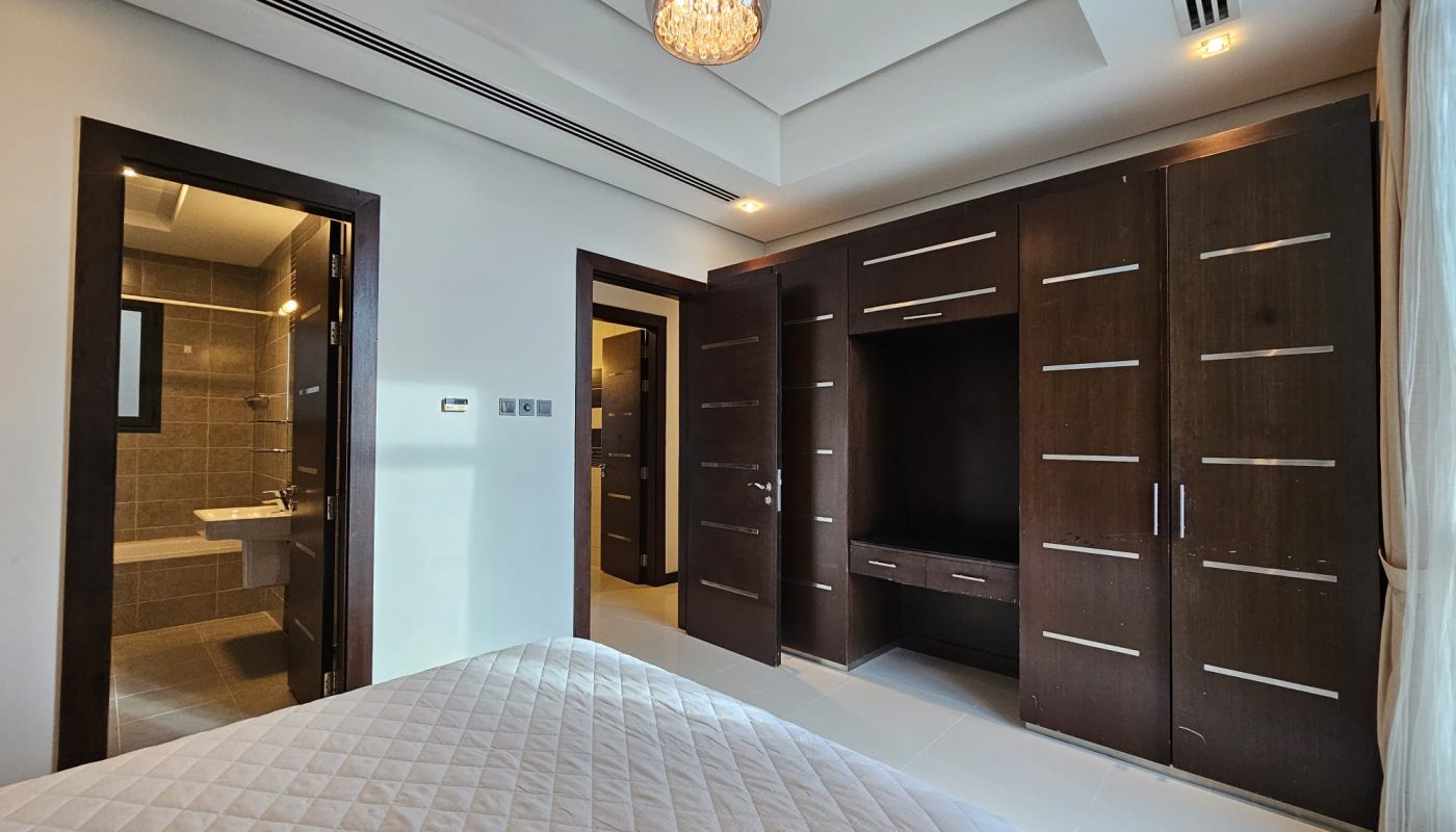 Modern 2 bedroom apartment for rent with a large bed, dark wooden cabinets, and an open door leading to an ensuite bathroom. Brightly lit with natural light and a pendant light.