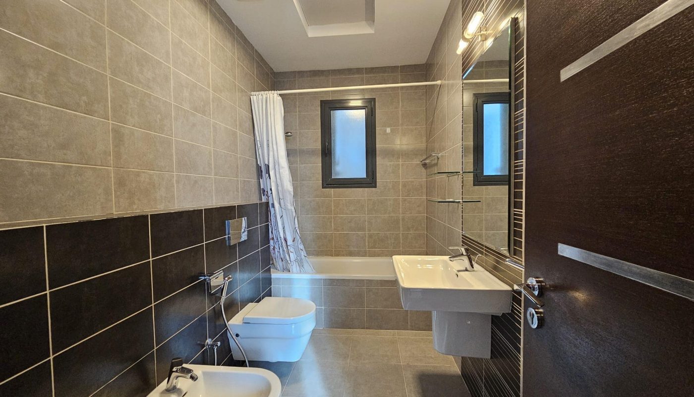 For Rent: Fully-furnished 2-bedroom apartment with a modern bathroom featuring beige and brown tiles, a bathtub, shower, sink, bidet, and a mirror.