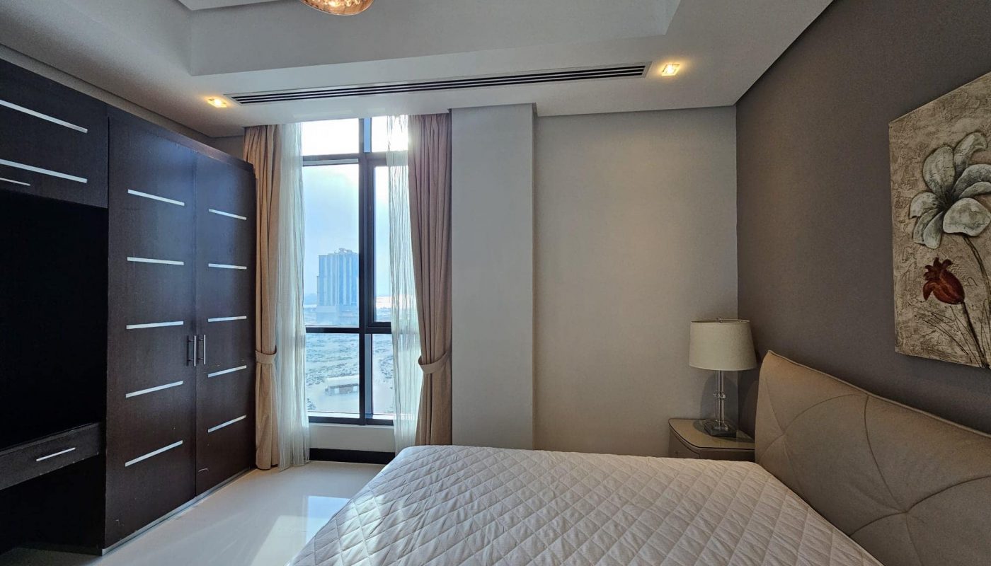 Modern 2-bedroom apartment for rent with a large bed, a dark wardrobe, floor-to-ceiling window with city view, and a decorative flower painting on the wall.