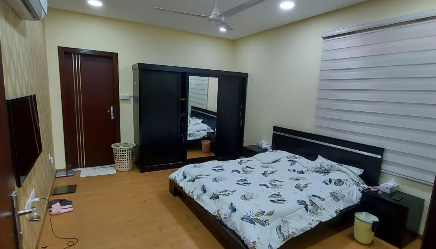 Modern bedroom in a family 3BR villa, featuring a large bed covered in a floral blanket, ceiling fan, wooden floor, and built-in wardrobes.