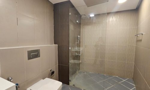 Modern flat bathroom interior with beige tiles, a glass shower enclosure, and a toilet on the left side.