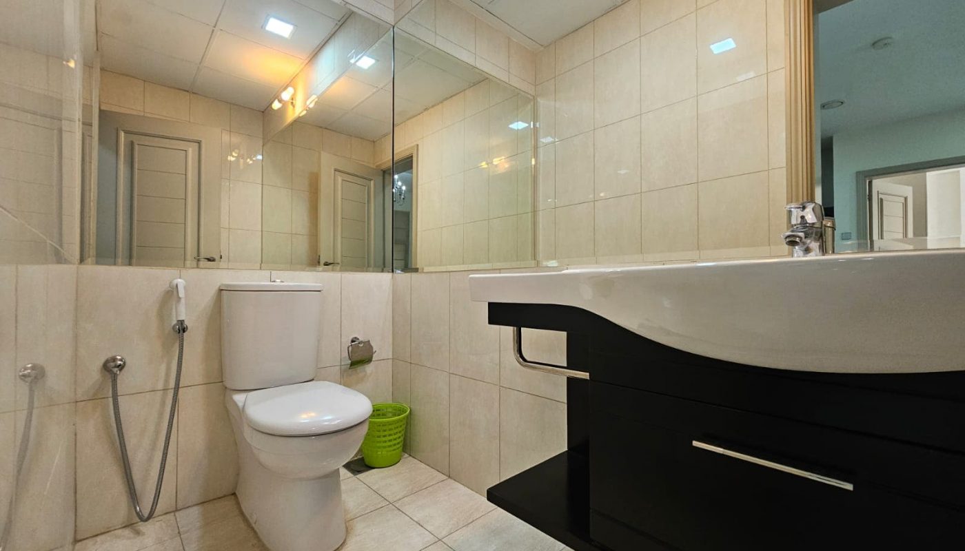 Modern bathroom interior in a 2-bedroom Adliya apartment with a white toilet, beige tiles, a large mirror, and a black vanity cabinet.