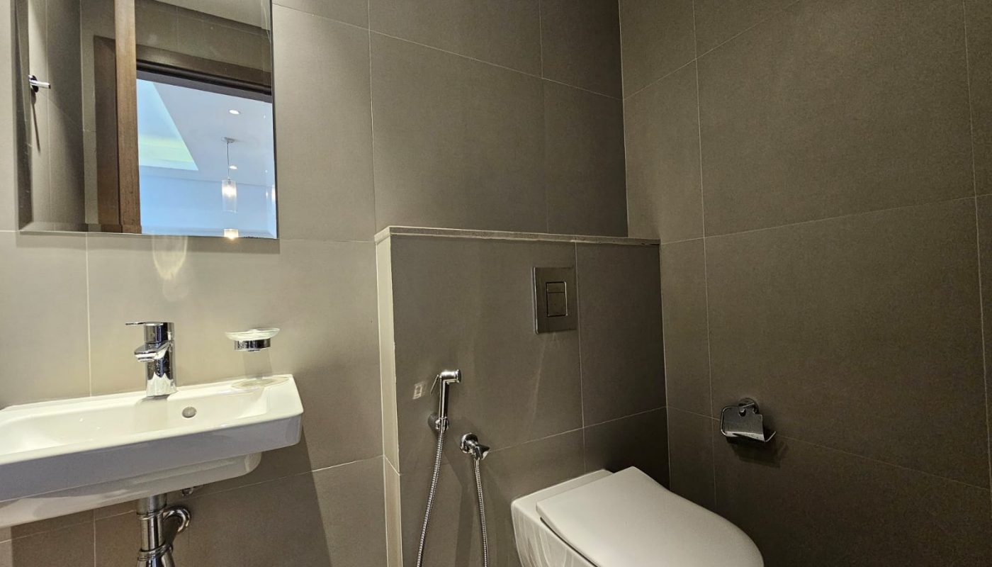 Modern bathroom interior with a wall-mounted sink, toilet, hand-held shower, and a small window above the sink.