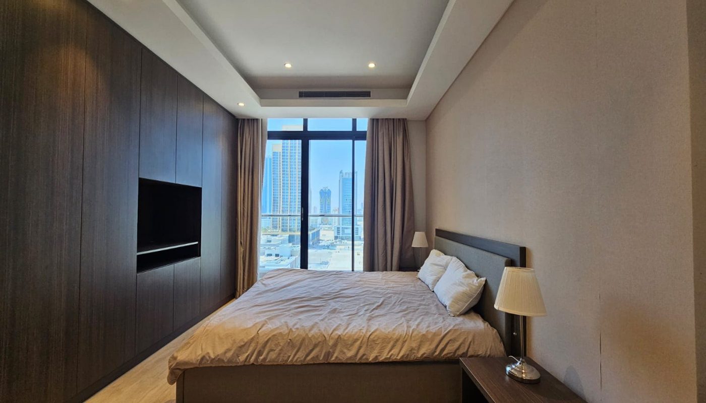 Modern bedroom with a large bed, wooden furniture, mounted tv, and a window with a city view.