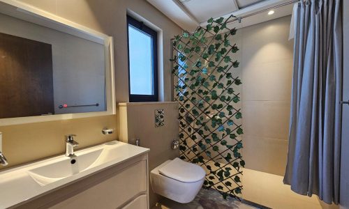 Modern bathroom with a sink, mirror, toilet, and shower area enclosed by a green leafy pattern curtain.