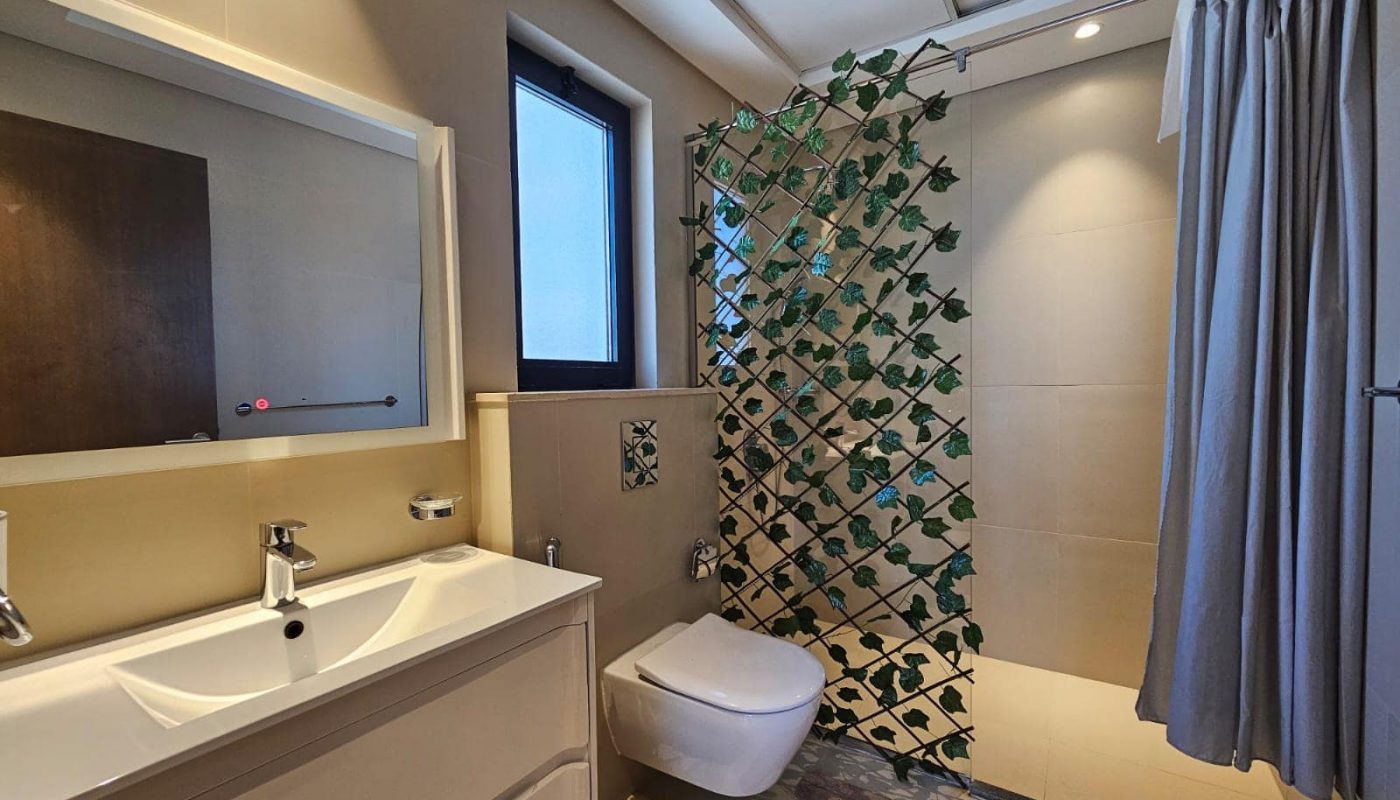 Modern bathroom with a sink, mirror, toilet, and shower area enclosed by a green leafy pattern curtain.