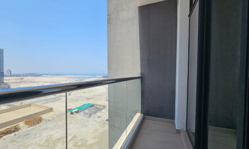 Balcony view from a high-rise building overlooking a construction site and beach in the distance, with clear skies.