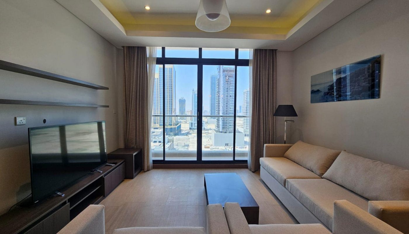 Modern flat with beige sofas, a flat-screen TV, and floor-to-ceiling windows overlooking a cityscape.