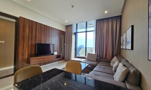 Modern living room in a Juffair flat with a large sectional sofa, marble table, wooden TV cabinet, and floor-to-ceiling window with curtains.