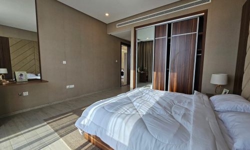 Modern hotel room featuring a neatly made bed, wooden furnishings, and a view into an adjoining bathroom in Juffair.