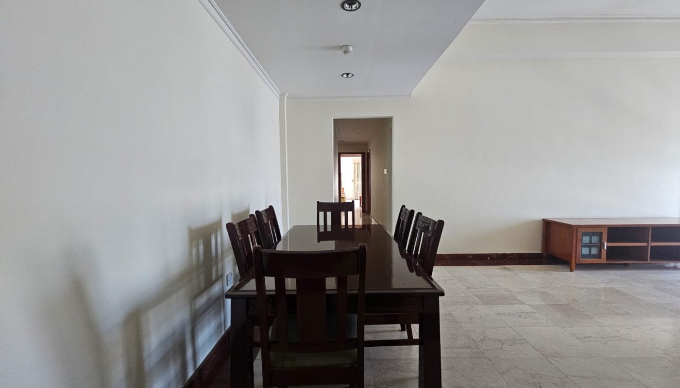 Empty dining room with a wooden table and chairs set in the center, marble flooring, and a doorway leading to another room in the background—ideal for a flat for rent in Seqya.