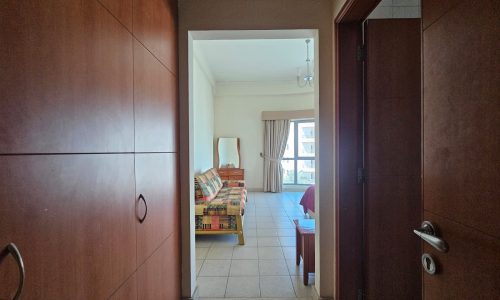 View from a hallway into a bright living room with a colorful couch and open balcony door in Seqya.