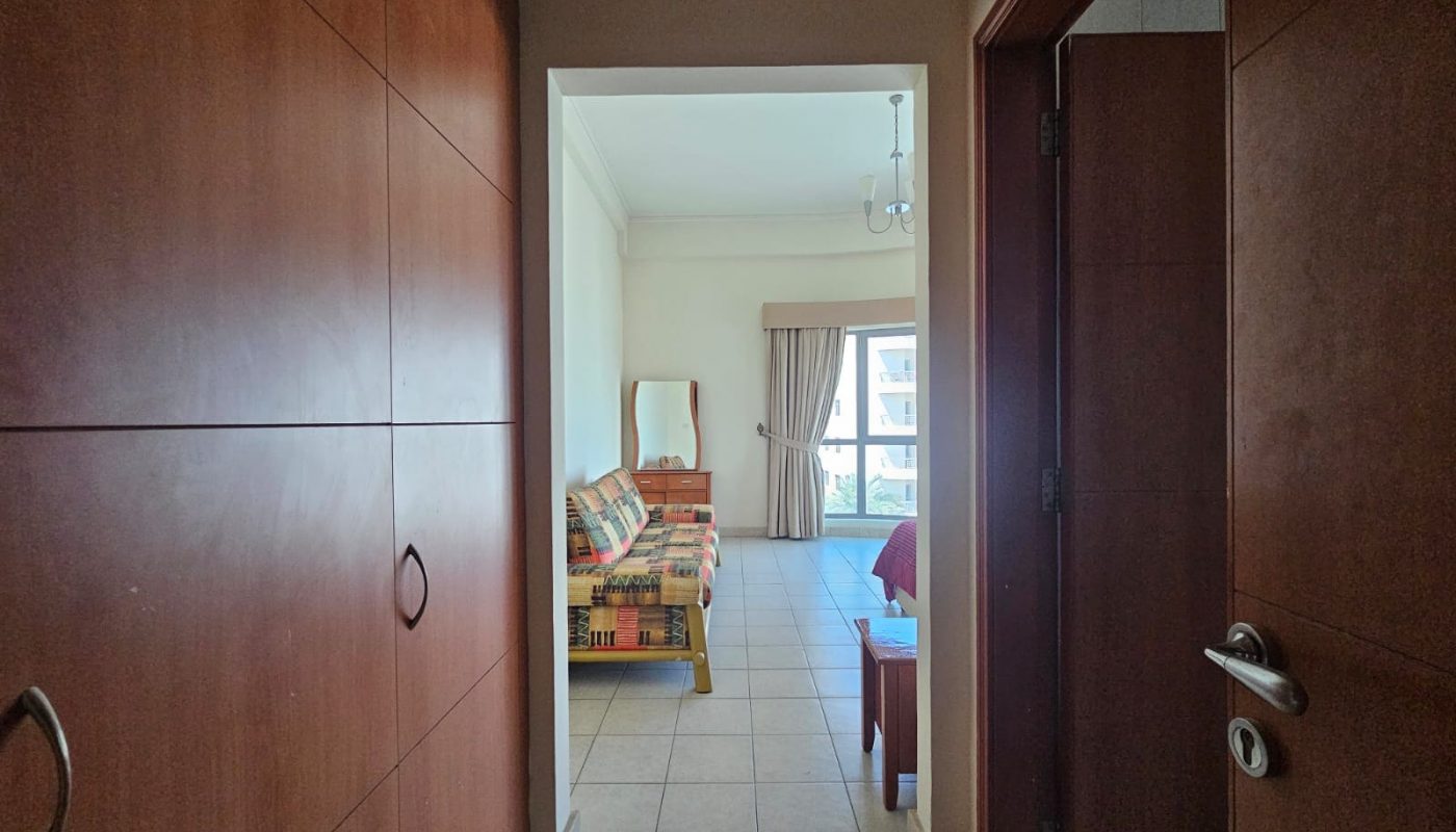 View from a hallway into a bright living room with a colorful couch and open balcony door in Seqya.