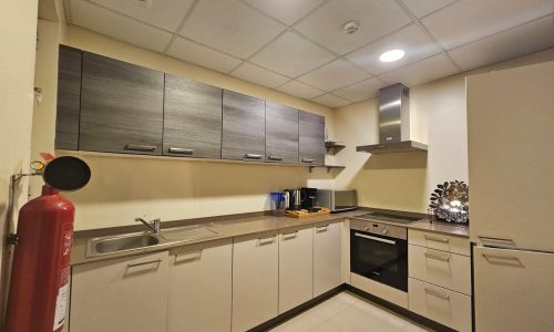 Modern kitchen interior in a fully furnished apartment with white cabinets, stainless steel appliances, a fire extinguisher, and under-cabinet lighting.