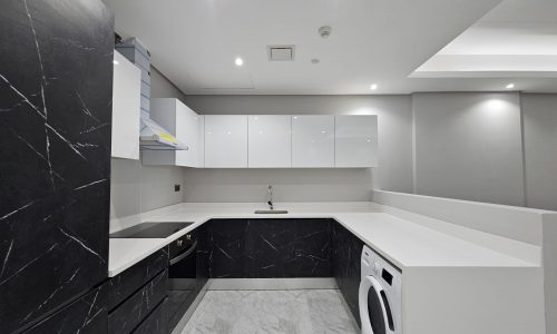 Modern kitchen with white countertops, black marble backsplash, white cabinets, and built-in appliances, including a washing machine.