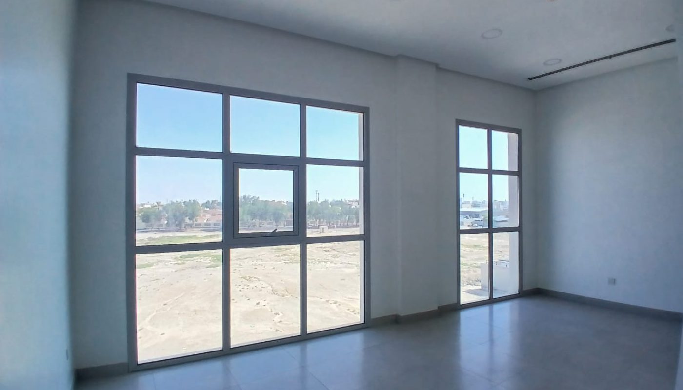 Empty room with large windows, tiled floor, white walls, and a view of an open area and trees outside.